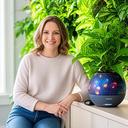 Lena aus Berlin vor einer hellen Pflanzenwand mit einem Orbit-Übertopf auf dem Sideboard